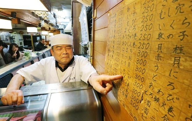 Kazuyoshi Ueno mostra o quadro com os preços escrito à mão pela esposa. Foto: Mainichi